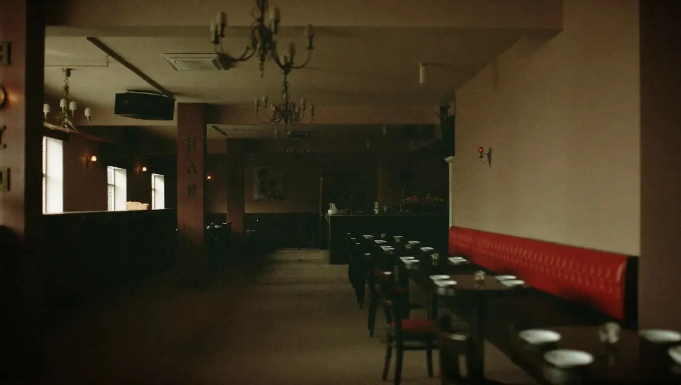 The dining room seen wide and empty, red banquettes and dark tables under warm chandelier light.